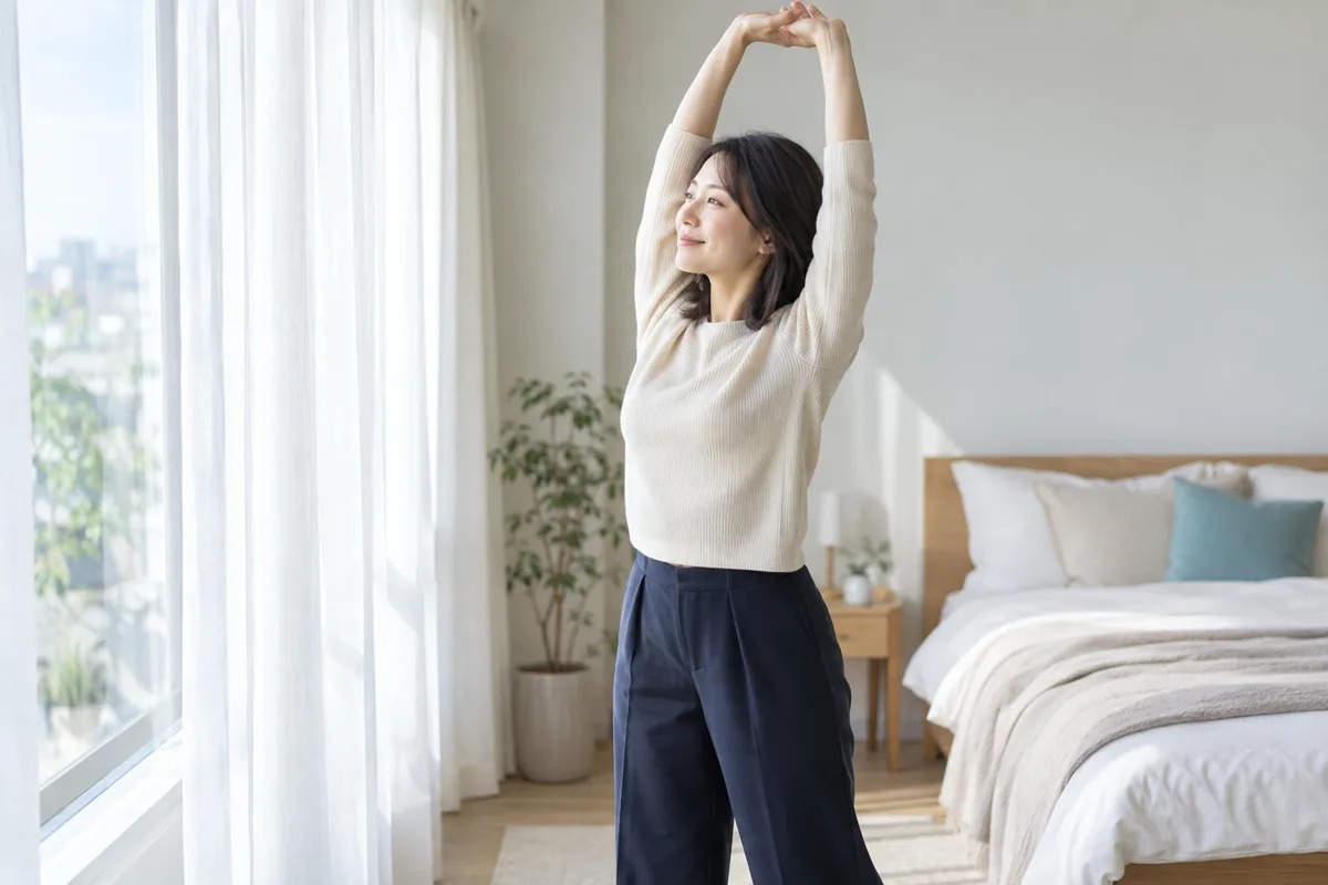 朝、窓辺で軽く伸びをする女性